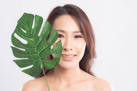 Close-up studio shot, Beautiful young woman with clean fresh skin holding green leaves. Proposing a product. Gestures for advertisement isolated on white background.の写真素材