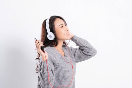 Young beautiful woman wearing a gray sweater is lying and listening to music wearing white music headphones isolated on white background. She is relaxing and happinessの写真素材