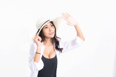 Portrait of a happy young woman in beach hat, swimsuit and white shirt at studio shot with sunlight isolated on white background. Summer travel concept.の写真素材