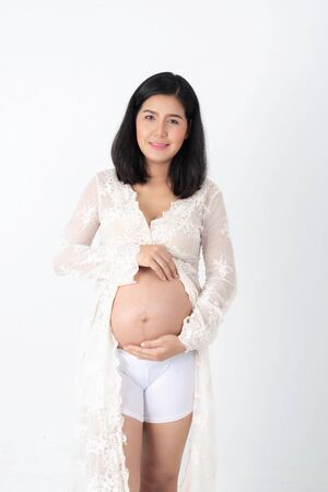 Pregnant happy Woman touching her belly. Pregnant young mother portrait, caressing her belly and smiling close-up. Healthy Pregnancy concept, brunette expectant female isolated on white background.の写真素材