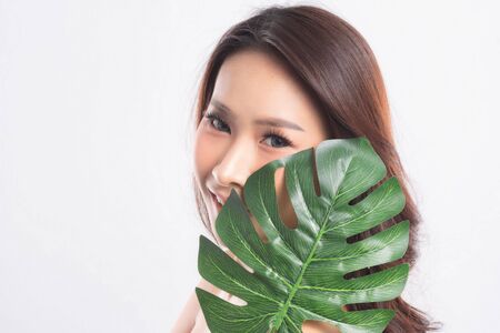 Close-up studio shot, Beautiful young woman with clean fresh skin holding green leaves. Proposing a product. Gestures for advertisement isolated on white background.の写真素材