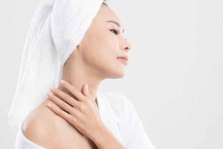 Beautiful young woman wearing bathrobe with towel on head with healthy skin is touching her skin with satisfaction is at studio shot isolated on white background.の写真素材