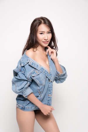 Beautiful asian woman with long brown hair wearing blue jeans jacket with no bra is sexy fashion position studio shot isolated on white background.の写真素材