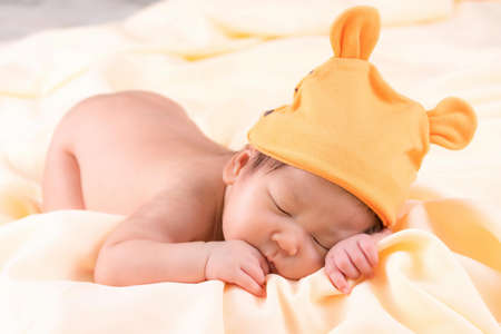 Portrait of a one month old sleeping, newborn baby girl. She is wearing a orange wool hat and sleeping on a cream blanket. Concept portrait studio fashion newborn.の写真素材