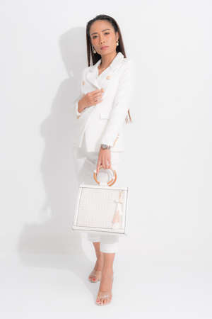 Fashion style catalog clothing for business woman black long hair natural make up wear white suit costume perfect body shape suit, carrying white bag at studio shoot on white background and shadow.の写真素材