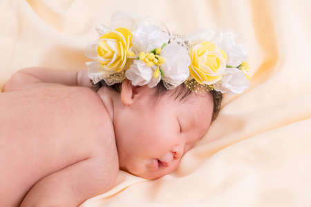 Portrait of a one month old sleeping, newborn baby girl. She is wearing a flower crown and sleeping on a cream blanket. Concept portrait studio fashion newborn.の写真素材