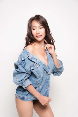 Beautiful asian woman with long brown hair wearing blue jeans jacket with no bra is sexy fashion position studio shot isolated on white background.の写真素材