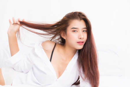 Beautiful young pretty asian woman wake up and stretching with white shirt at the white bed in the morning.の写真素材