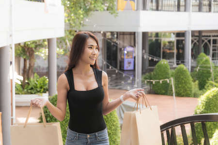 Beautiful woman wearing a black shirt and jeans perfect body shape, is walking up the stairs with carrying shopping bag at outdoor shopping mall in day time.の写真素材