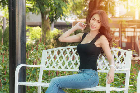 Beautiful woman wearing a black shirt and jeans perfect body shape, is sitting in a chair with a shopping bag at outdoor shopping mall in the evening when the red light shines.の写真素材