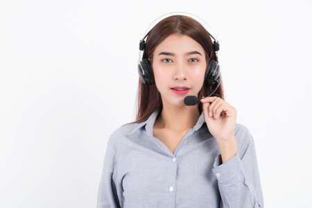Portrait of happy smiling female customer support phone operator short hair, wearing a white shirt with headset standing one side holding the earphone isolated on white background.の写真素材