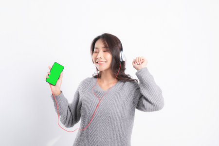 Young beautiful woman wearing a gray sweater is lying and listening to music wearing white music headphones isolated on white background. She is relaxing and happinessの写真素材