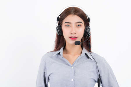 Portrait of happy smiling female customer support phone operator short hair, wearing a white shirt with headset standing one side holding the earphone isolated on white background.の写真素材
