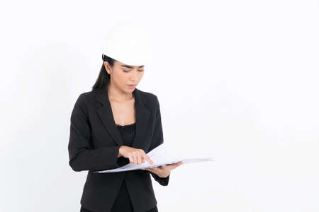 Portrait young engineer woman wearing black suit and white safety-helmet looking at blueprint in hand, shot studio isolated on white background.の写真素材