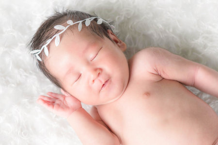 Portrait of a one month old sleeping, newborn baby girl. She is wearing a crown headband and sleeping on a white blanket. Concept portrait studio fashion newborn.の写真素材