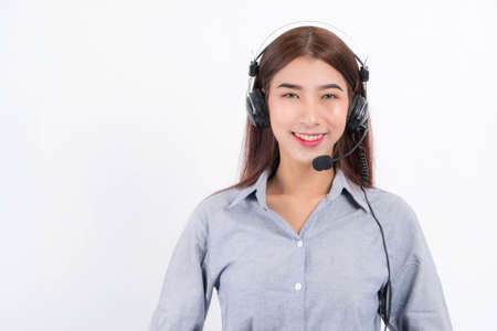 Portrait of happy smiling female customer support phone operator short hair, wearing a white shirt with headset standing one side holding the earphone isolated on white background.の写真素材