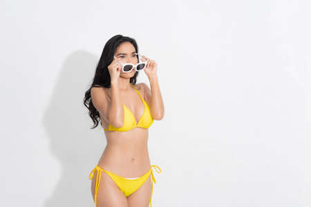 Beautiful woman in happiness wearing a yellow bikini dress and holding white sunglasses post in concept summer fashion studio shoot isolated on white background.の写真素材