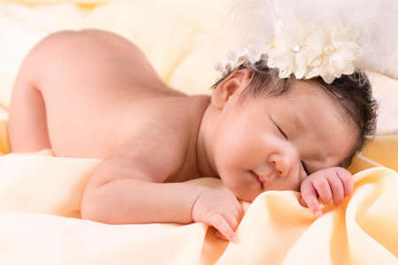 Portrait of a one month old sleeping, newborn baby girl. She is wearing a flower crown and sleeping on a cream blanket. Concept portrait studio fashion newborn.の写真素材