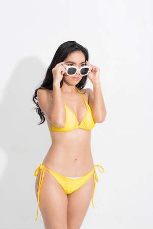 Beautiful woman in happiness wearing a yellow bikini dress and holding white sunglasses post in concept summer fashion studio shoot isolated on white background.の写真素材