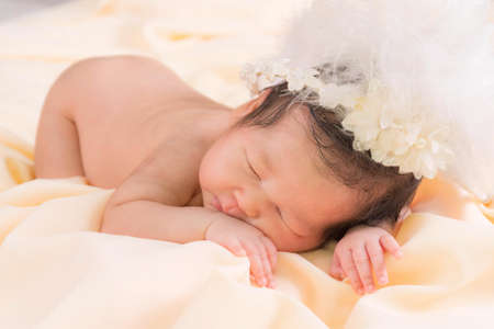 Portrait of a one month old sleeping, newborn baby girl. She is wearing a flower crown and sleeping on a cream blanket. Concept portrait studio fashion newborn.の写真素材