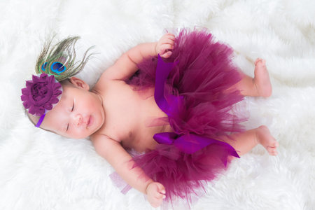 Portrait of a one month old sleeping, newborn baby girl. She is wearing a purple crown headband and sleeping on white fur. Concept portrait studio fashion newborn.の写真素材