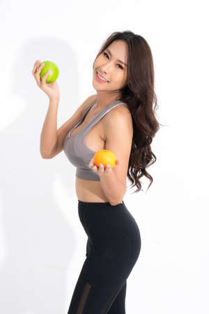 Beautiful asian young woman healthy food wearing workout clothes holding green apple and orange with healthy food isolated on a white background.の写真素材
