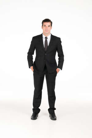 Portrait of a smiling western business man wearing a black suit with his hands in his pants pocket at studio shot on white background.の写真素材