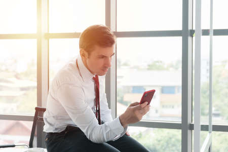 Business man in formal clothing using mobile phone at work in the evening when the sun shines through the office.の写真素材