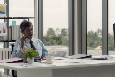 Senior businessman sitting at his desk in the office, thinking and thinking and feeling anxious.の写真素材