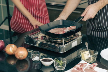Close-up shot of couple cooking a steak on the stovetop.の写真素材