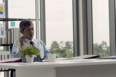 Senior businessman sitting at his desk in the office, thinking and thinking and feeling anxious.の写真素材