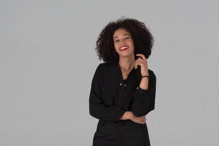 A vibrant portrait of a young African American woman with curly hair, happily laughing and expressing genuine joy studio on gray background.の写真素材