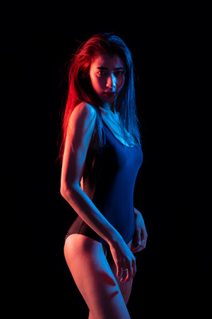 Fashion portrait striking image of a woman in a dark bathing suit, lighting color half lit in red and half in blue studio shot on black background.の写真素材