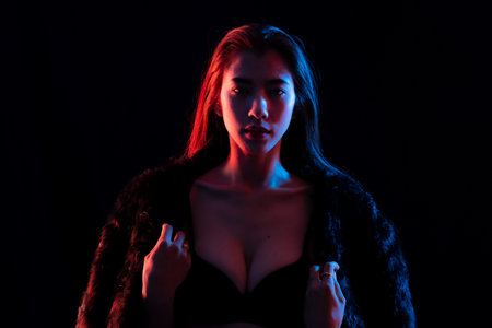 Fashionable sensual studio portrait woman wearing black lingerie and a fur coat, illuminated blue...