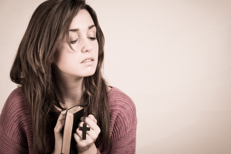 Christian woman with closed eyes holding a cross and a psalm book  