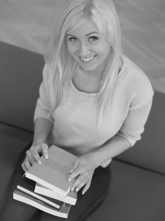Smiling woman sitting holding a stack of booksの写真素材