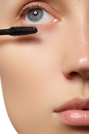 Mascara applying close-up, long lashes. Mascara brush. Eyelashes extensions. Make-up for blue eyes. Eye make up apply. Young beautiful woman applying mascara makeup on eyes by brushの写真素材