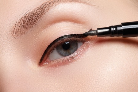 Beautiful model applying eyeliner close-up on eyeの写真素材