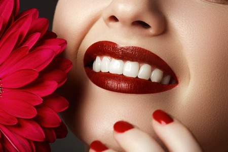 Close-up shot of sexy woman lips with red lipstick and beautiful pink flower. Perfect clean skin, fashion lip make-up. Beautiful spa portrait with tender pink  flower. Spa and cosmeticsの写真素材