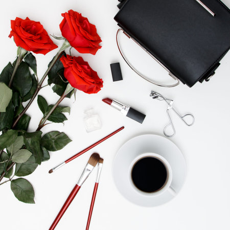 Decorative flat lay composition with cosmetics, womens accessories and flowers. Flat lay, top view on white background. A cup of coffee and a fashionable clutch on a white tableの写真素材