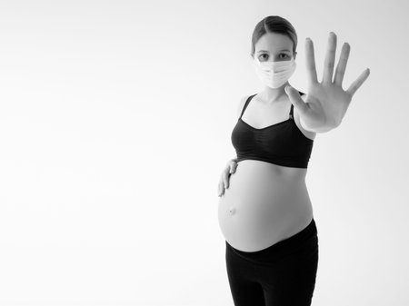 Pregnant woman wearing face mask protective for spreading of disease virus. A pregnant woman wears a...