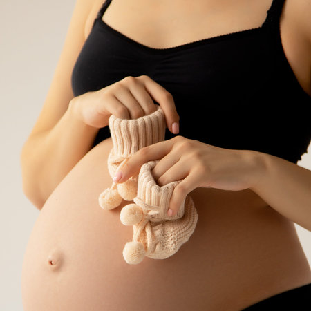Small shoes for the unborn baby in the belly of pregnant woman. Close up. Motherhood, pregnancy,...