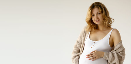 Woman standing and touching with hands her big belly. Isolated on gray background. Emotional loving...