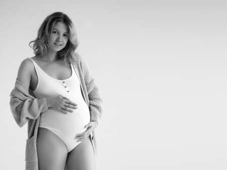 Woman standing and touching with hands her big belly. Isolated on gray background. Emotional loving pregnancy time - 37 weeks. Baby expectation. Love, happiness and safety concept. Closeupの写真素材