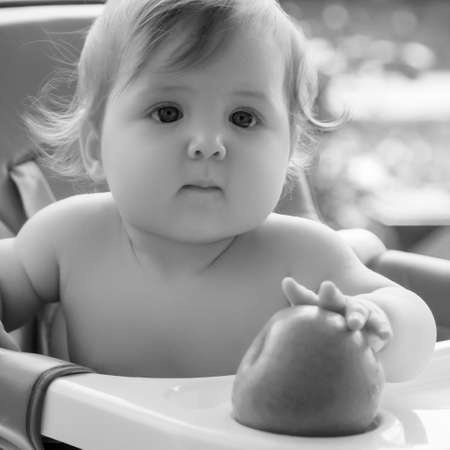 little smiling girl sits in baby-chair and have a breakfast. baby with big eyes and red curly hair eats at a table. Summer vacation concept. The emotionsの写真素材