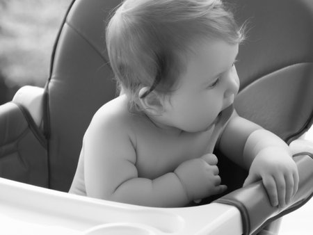 Happy baby sitting in high chair eating puree outdoors. Close up. Copy space. Healthy nutrition for kids concept. little smiling girl sits in baby-chair and have a breakfast. baby eats at a tableの写真素材