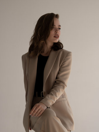 A fashionable young girl. A female model, a studio shoot. A beauty in a beige jacket on a gray background. Fashion and Beauty Photographyの写真素材