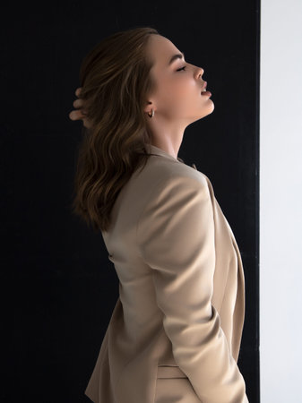 Elegant style. A beautiful fashion model poses in a loose beige pantsuit on a white background....