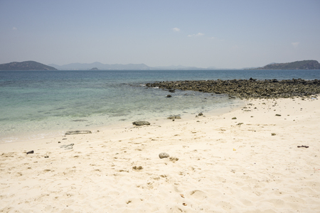 Blue sea with white beach and mountain in background.の写真素材