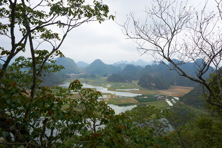 Field between mountain range from viewpoint of peak mountain that trees in foreground in cloudy day at Puzhehei, Yunnan, China.の写真素材